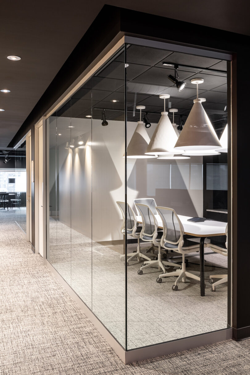 A conference room with a white conference table illuminated by white pendant lamps