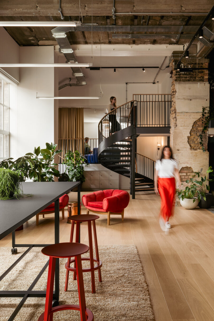 A modern office with a wooden floor, red stools, and a spiral staircase