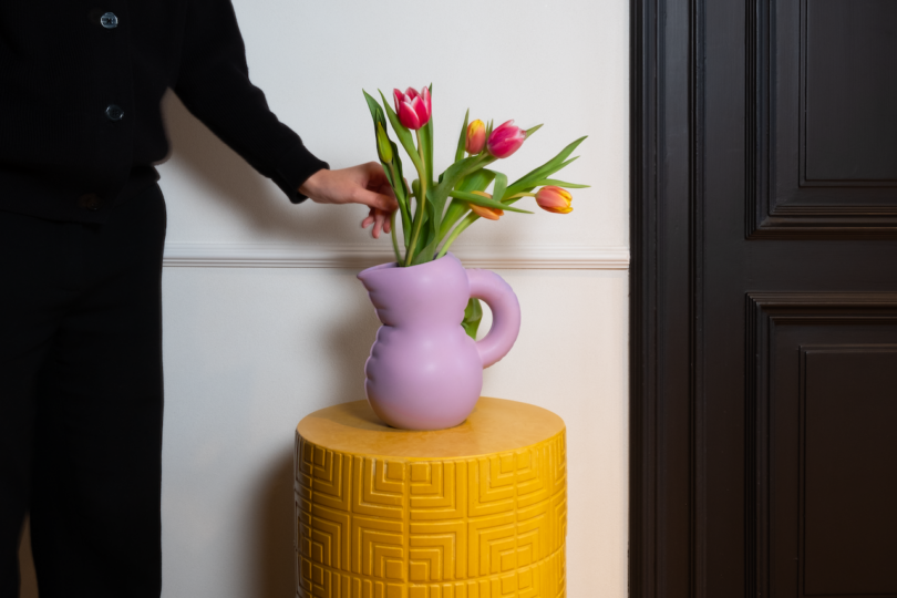 Person arranging tulips in a purple vase on a yellow side table.