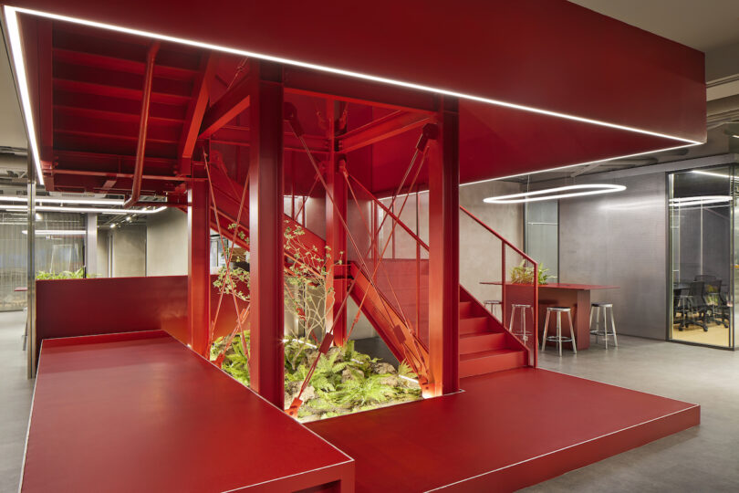 Intérieur de bureau moderne doté d'un escalier rouge saisissant avec verdure intégrée, entouré d'un espace de travail de style industriel.