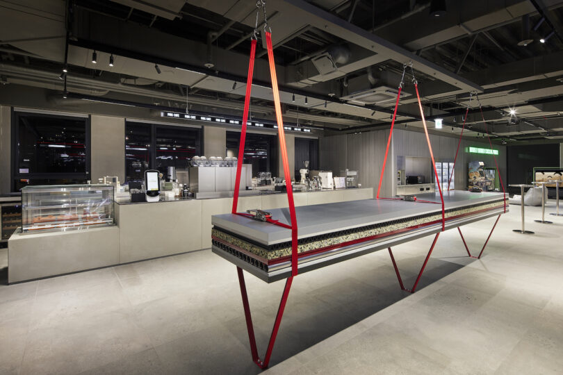 A modern and spacious interior of a cafe with an unconventional table suspended by red straps.