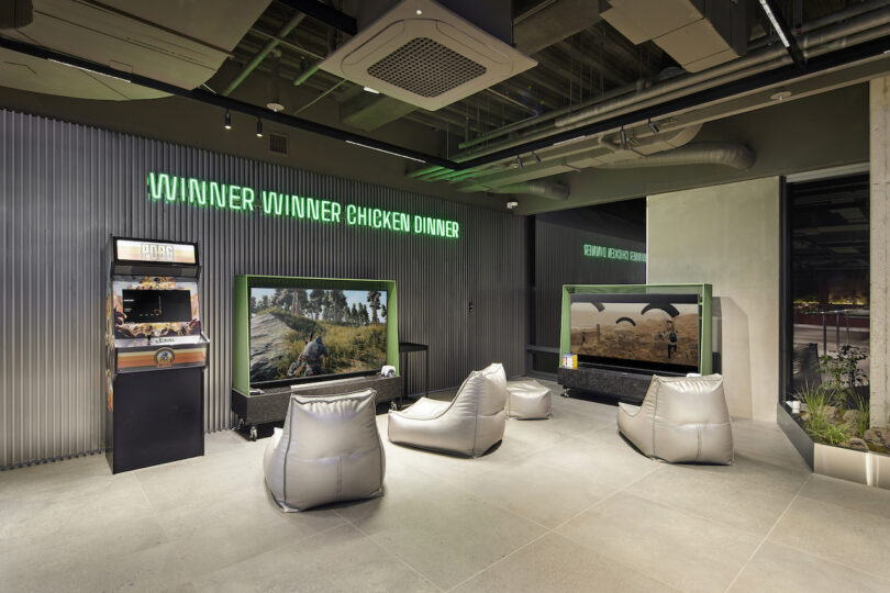 Modern gaming lounge with bean bags and large screens displaying "winner winner chicken dinner" signage.
