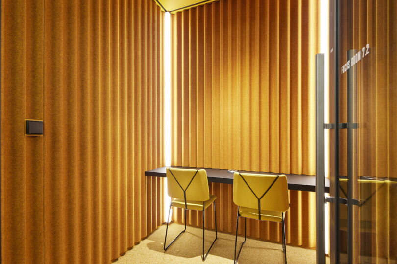 Modern meeting room with yellow curtains and accent walls, featuring two chair and table set on a matching carpet.