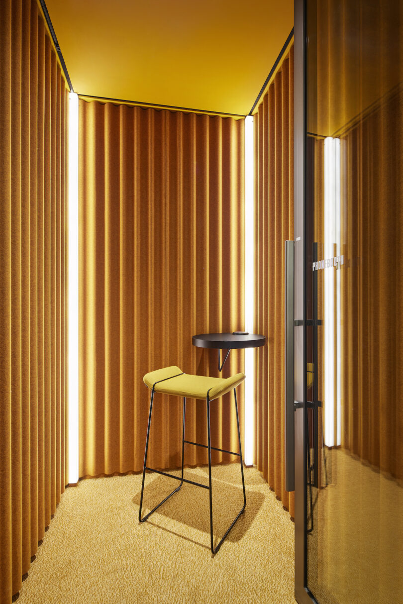 Salle de réunion moderne avec des rideaux jaunes et des murs d'accent, comprenant une seule chaise et une table posées sur un tapis assorti.