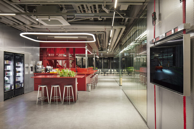 Modern office break room with red accents, bar-style seating, and exposed industrial ceiling.