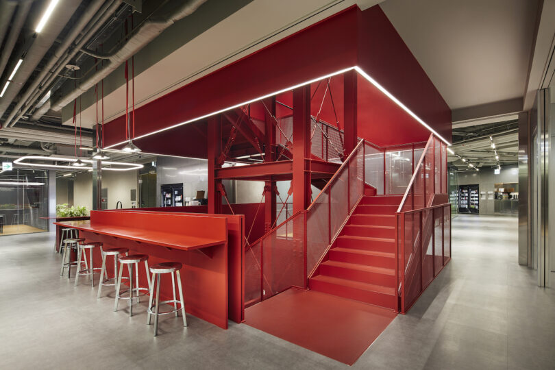 Modern office interior featuring a vibrant red staircase and matching bar-style counter with stools.
