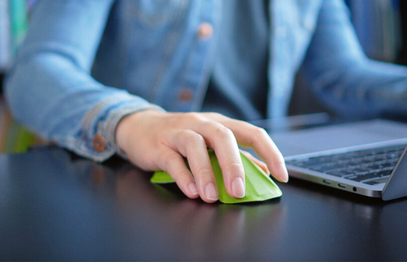 A person is using a green computer mouse on a black desk.