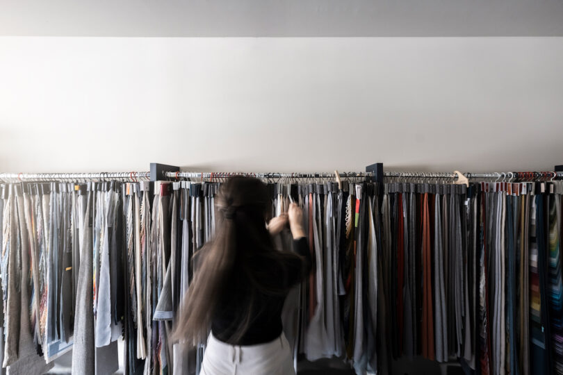 زنی در حال مرور لباس‌های NOA روی قفسه‌های فروشگاه.