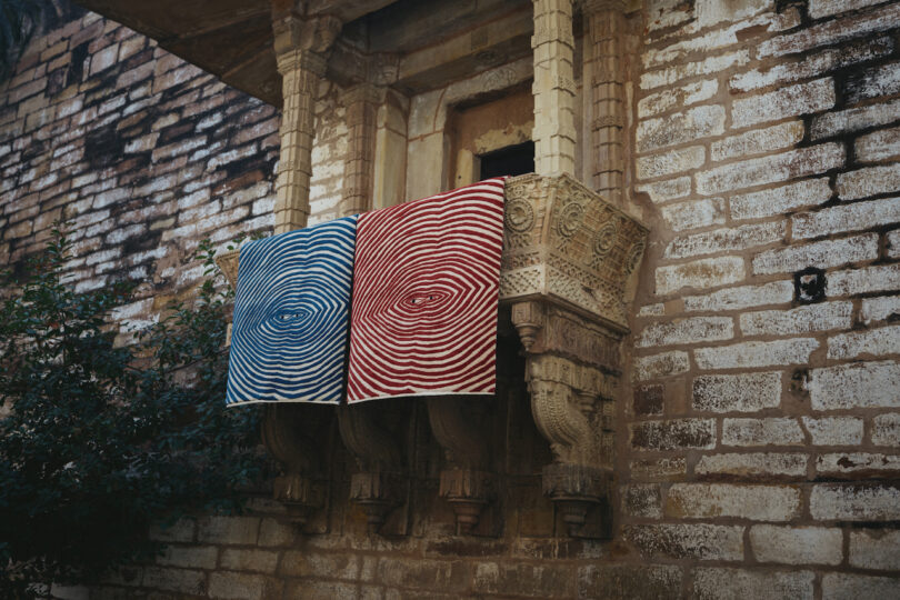 a blue and a red rug hung on a balcony of a brick building