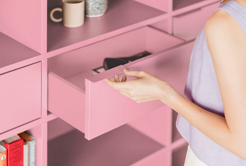 closeup of a woman's hand opening a drawer on a modern pink shelving unit
