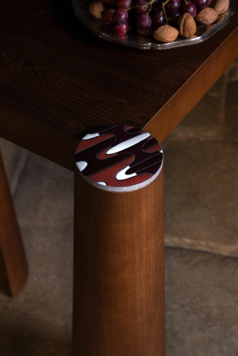 Detalhe de uma longa mesa de madeira com grossas pernas cilíndricas.