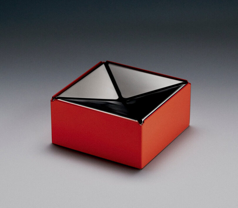 A red and black geometric cannabis ashtray with a glossy finish and X-shaped opening, set on a gray gradient background.