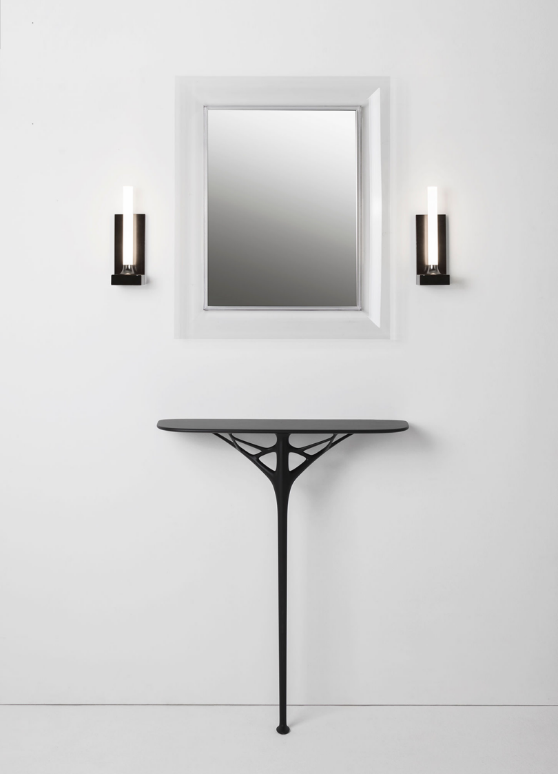 A modern hallway featuring a sleek, wall-mounted console table with a framed mirror above it, flanked by two candle sconces.