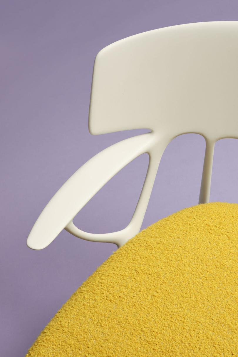 Modern white chair partially shown against a purple background with a yellow textured surface in the foreground.