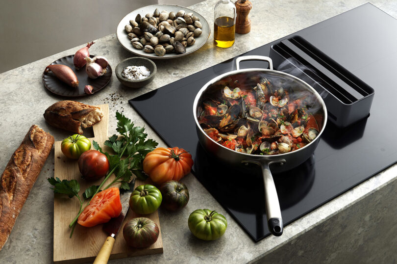 Sauté pan with seafood on an induction stove, surrounded by fresh ingredients.