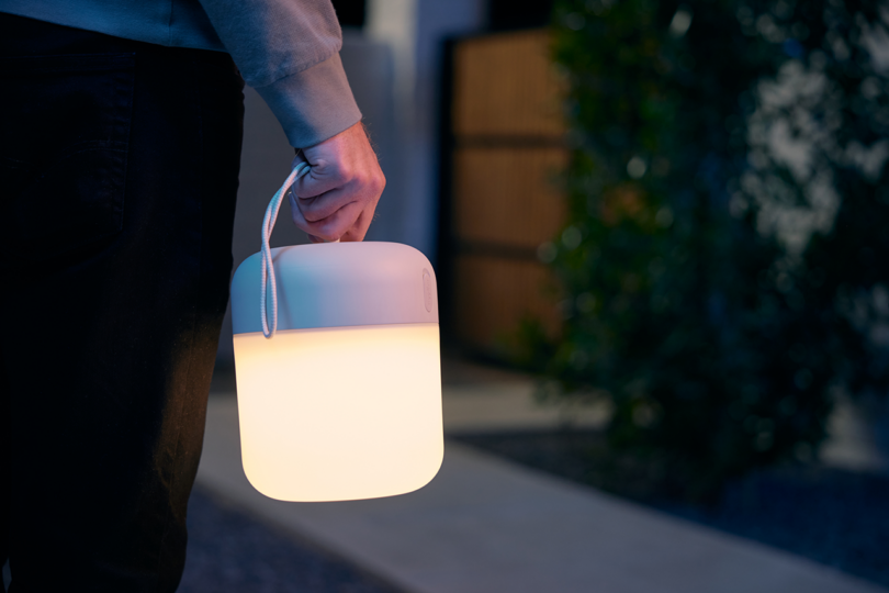 Person carrying a portable lamp outdoors at dusk.