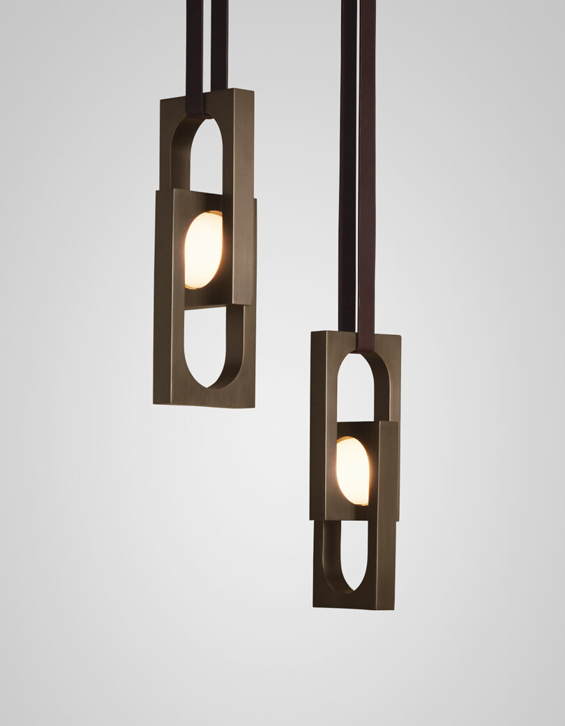 Duas luminárias pendentes modernas com molduras geométricas, penduradas sobre um fundo cinza claro.
