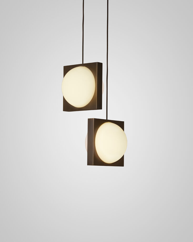 Two modern pendant lights with square frames and opaque globes, hanging against a light gray background.