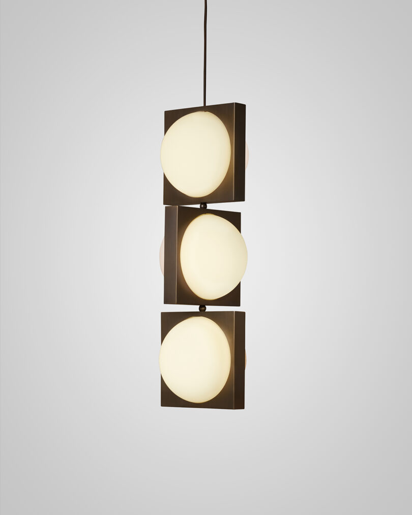 Three modern pendant lights with square frames and opaque globes, hanging against a light gray background.