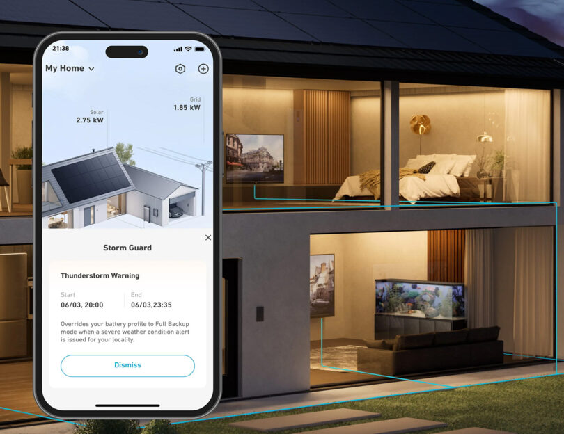 Smartphone displaying a home energy management app with a storm warning notification, held in front of a stylish house interior during the evening, featuring the Anker SOLIX X1 residential battery status.