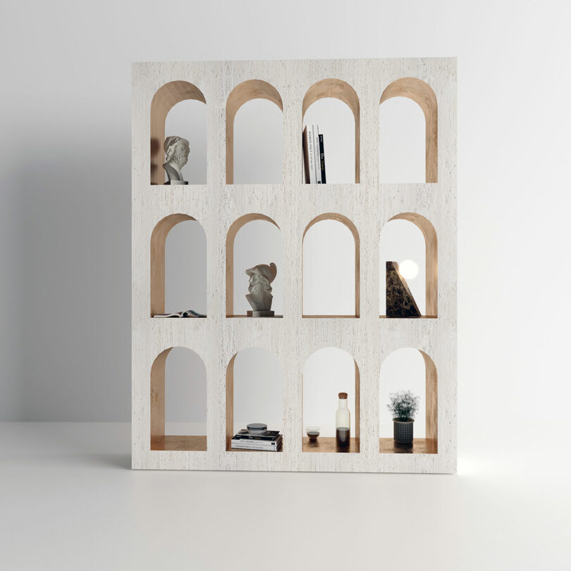 A contemporary marble shelving unit with multiple arch-shaped compartments, some containing books, sculptures, and decorative items.