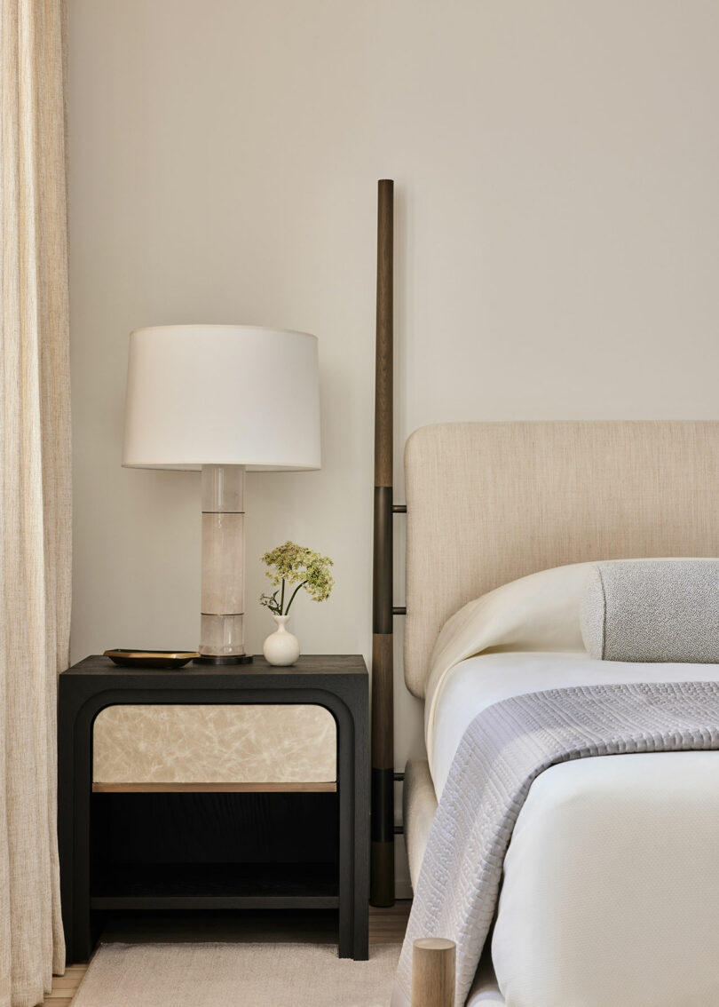 Elegant bedroom corner featuring a bedside table with a lamp, a small floral accent, and a neatly made bed.