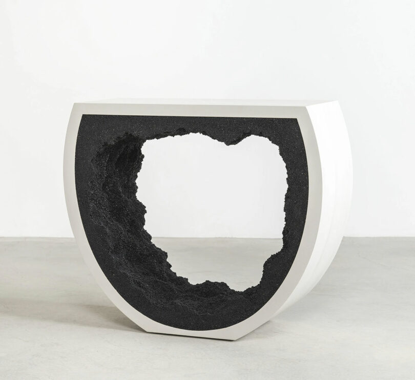 A modern, circular white bench with an arch-shaped cut-out section revealing a textured black interior.