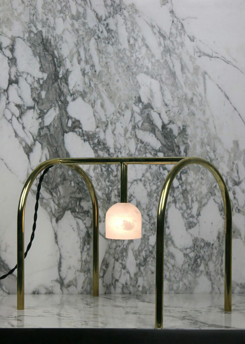 A modern lamp with a single bulb and an arched golden frame stands against a marble backdrop.