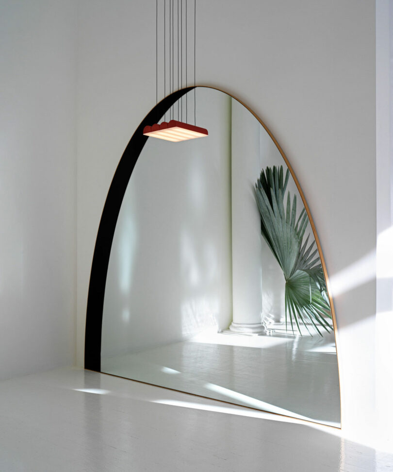 An arch floor lamp with a minimalist design casting light on a white wall next to a potted plant.