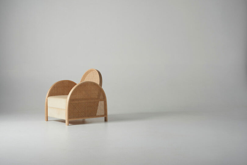 A minimalist wooden chair with an arching woven backrest against a plain background.