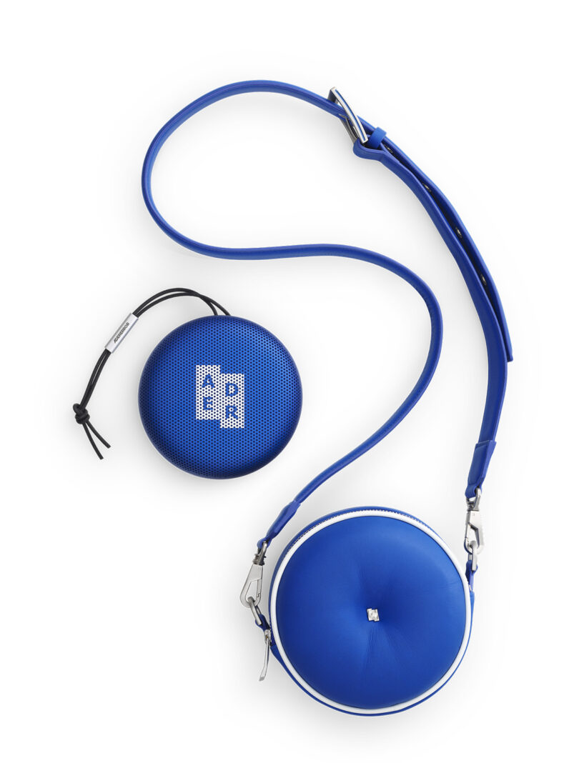 Blue circular crossbody bag with matching Bang & Olufsen's Beosound A1 ADER ERROR Edition Bluetooth speaker on a white background.