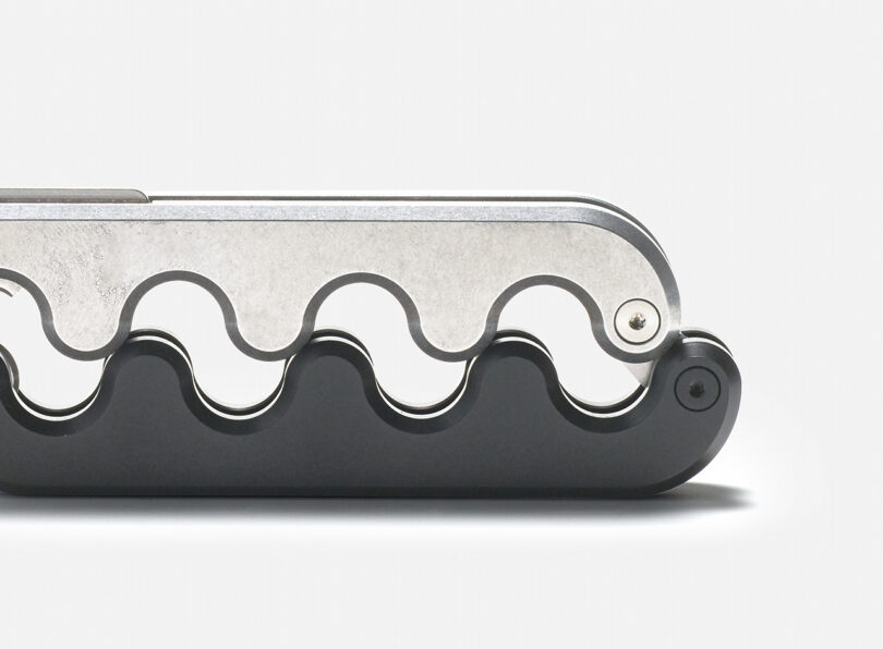Close-up of a Sidewinder pocket knife with a wavy interlocking hilt handle on a white background.