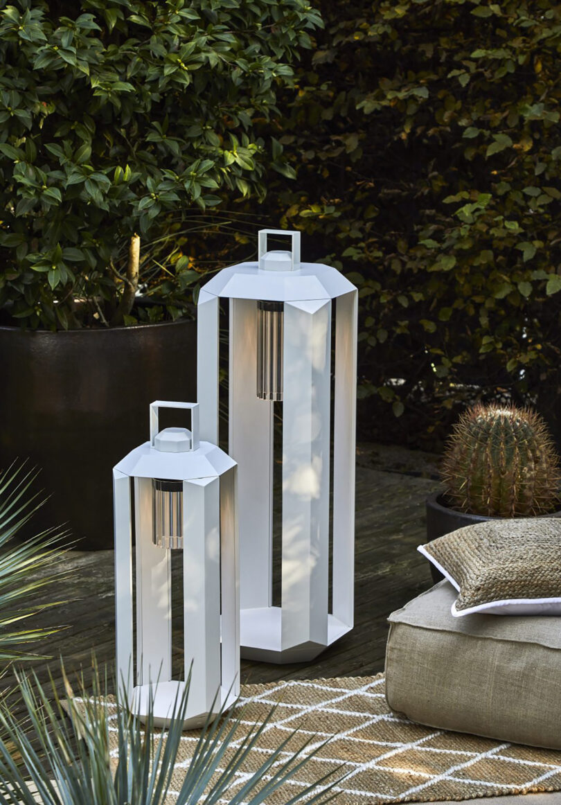 Duas modernas lanternas brancas ao ar livre em um pátio com jardim ao entardecer.
