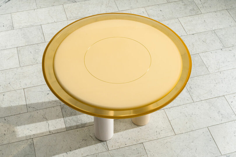 Top view of a circular yellow table designed by Djivan Schapira, centered on a tiled floor.