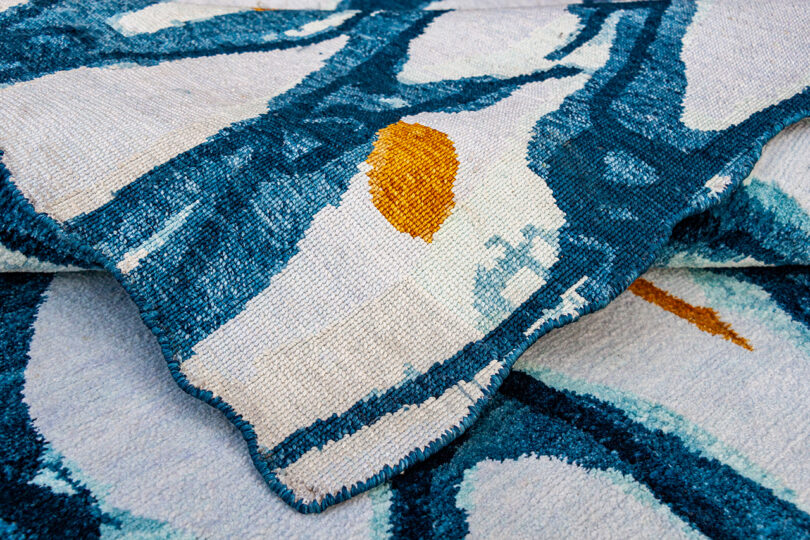 Close-up of a crumpled rug with abstract blue and white patterns and a prominent orange spot.