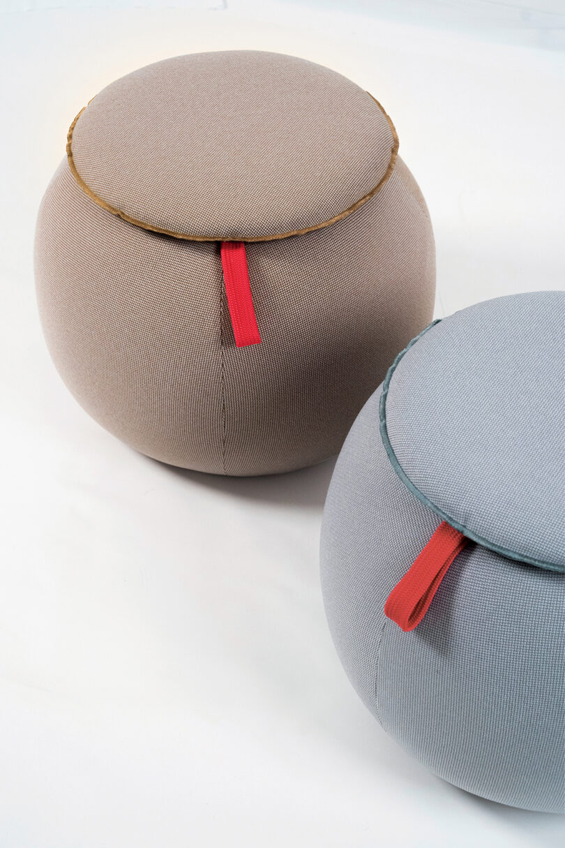 Two round poufs in beige and gray, each with a contrasting red handle on a white background.
