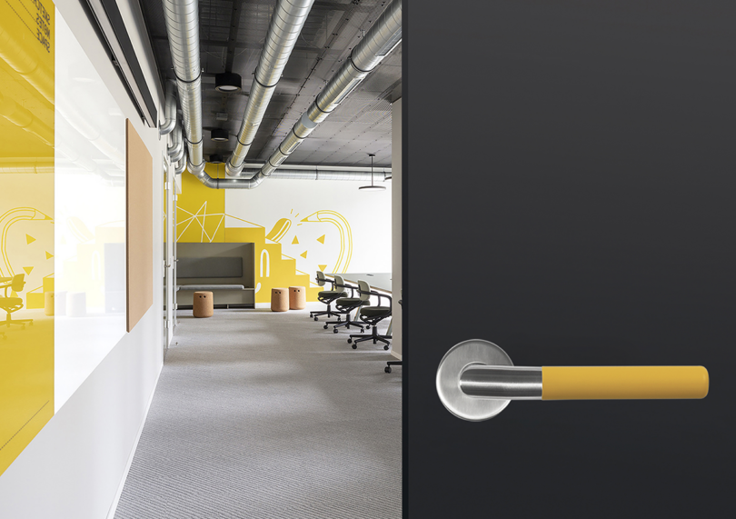 Modern office interior with yellow accents, exposed ductwork on the ceiling, and rows of desks and swivel chairs.