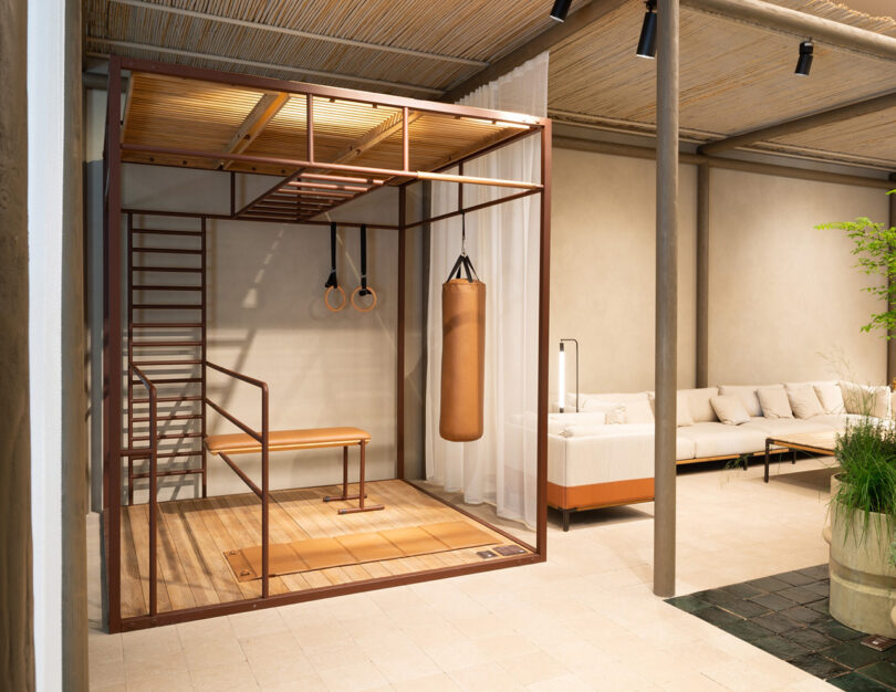 OUT-FIT home gym featuring a wooden floor, pull-up bars, a punching bag, and rings, set indoors in a lounge area with a couch and table.