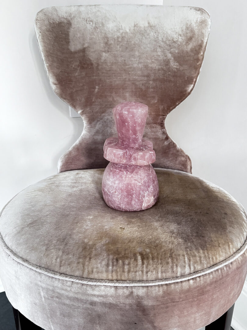 A velvet chair with a pink sculpture on its seat.