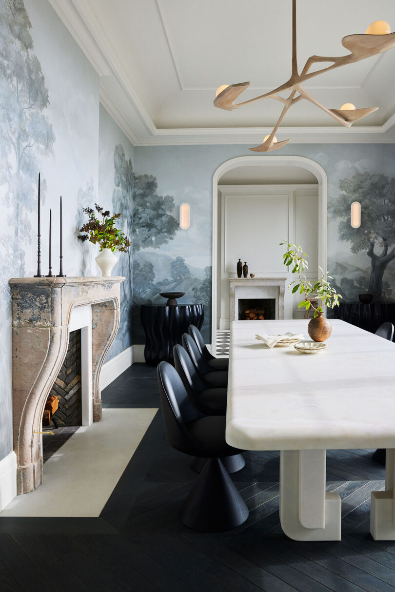 Dining room featuring a white marble table, black chairs, a stone fireplace, and walls with floral murals.