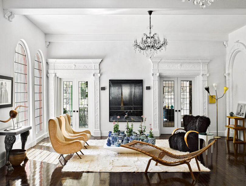 Living room with white walls, arched windows, a black door, and eclectic furnishings including a fur chair and modern lamps.