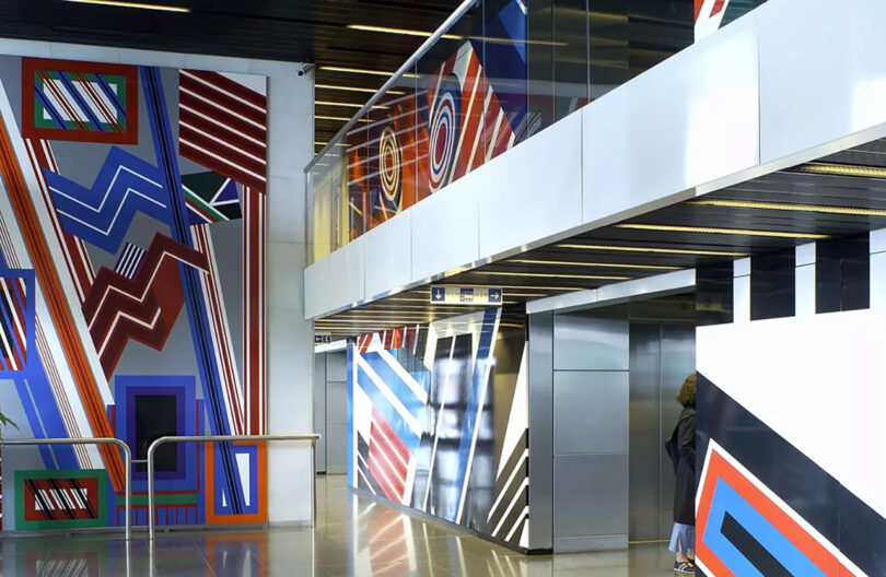 Interior of a modern building with bold geometric murals in red, blue, and white on walls and stairs, with one person walking.