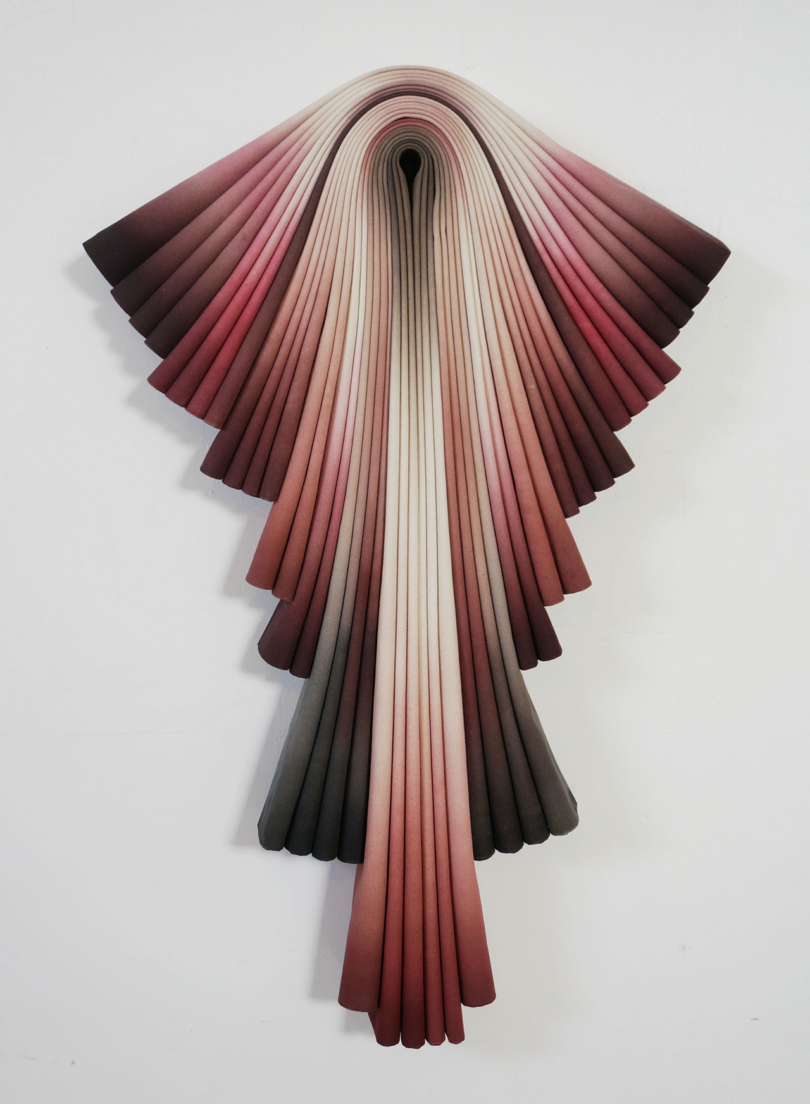 A wall-mounted sculpture resembling an abstract, cascading ribbon in varying shades from white to dark red.