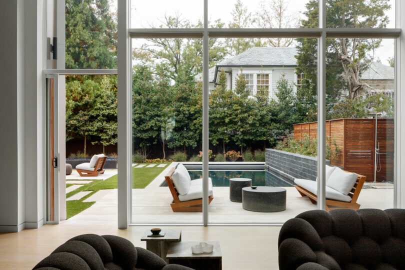 Modern living room with expansive glass walls overlooking a tranquil backyard.