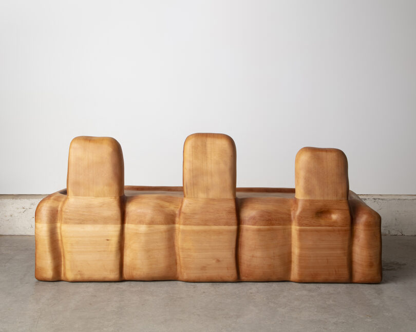 A wooden three-seater abstract sofa with smooth, rounded contours against a white background.