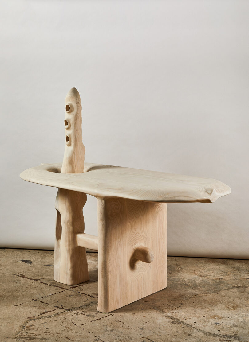 A wooden table with an abstract design featuring organic shapes and holes, set against a plain backdrop.