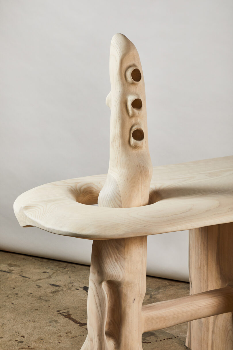 Detail of a wooden table with an abstract design featuring organic shapes and holes, set against a plain backdrop.