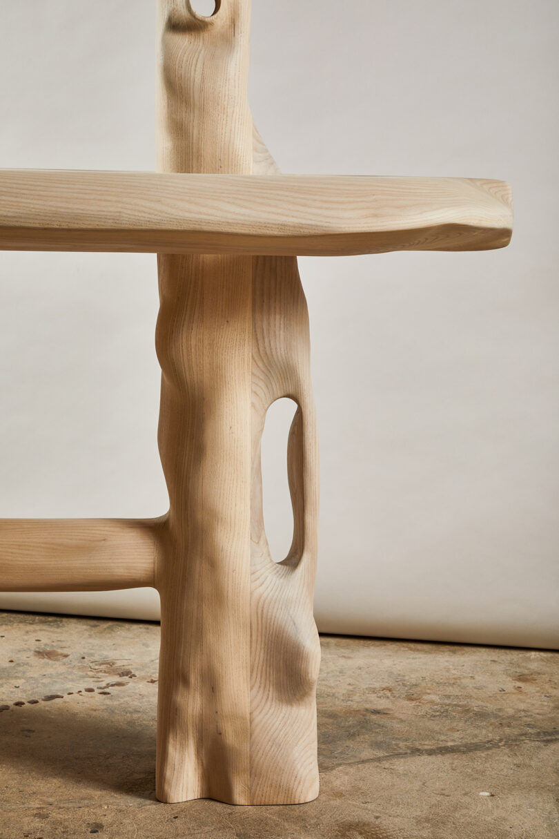 Detail of a wooden table with an abstract design featuring organic shapes and holes, set against a plain backdrop.