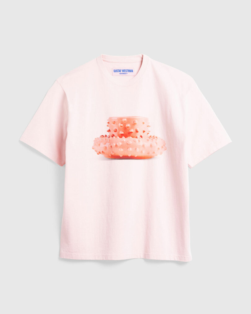 Pink t-shirt with a circular coral-shaped Gustaf WestmanGustaf Westman mug and saucer in the center on a plain background.