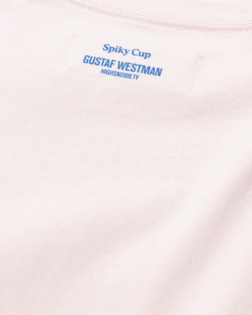 Close-up of a pink fabric with "spiky cup Gustaf Westman highsnobiety" text printed in blue.